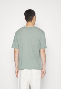 T-shirt en coton vert avec un col rond, des manches courtes et un ourlet droit. Présente une couture discrète au dos pour un détail de design supplémentaire.