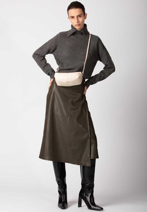 Maglione grigio in lana, gonna in pelle verde oliva e stivali neri con tacco a spillo fino al ginocchio. Piccola borsa a tracolla color crema e spacco laterale nella gonna.