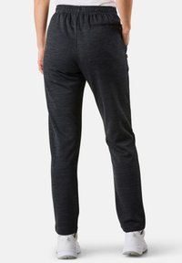 Svarta, melerade träningsbyxor med elastisk midja, sidofickor och en dragkedjeficka bak, smalnerande passform vid anklarna.