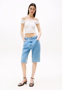 Fehér, vállatlan, textúrált kialakítású crop top, világoskék farmer berber nadrággal párosítva, amely zsebekkel és laza fit állással rendelkezik. Fekete, magas sarkú szandál.