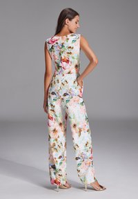 Blumiger Jumpsuit aus leichtem Stoff, mit einem bunten Blumenmuster auf weißem Hintergrund, ärmellos und mit seitlichen Taschen.
