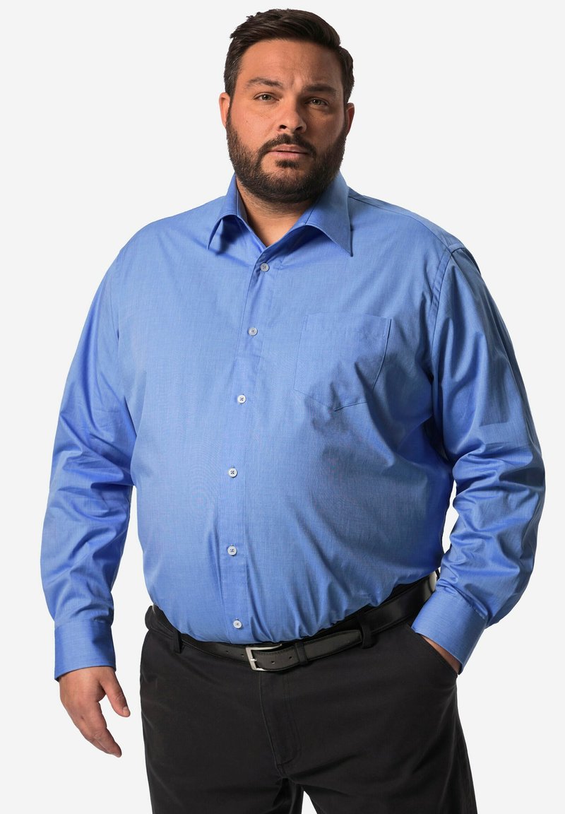 Camicia a maniche lunghe color azzurro chiaro realizzata in un tessuto texture, con bottoni frontali e una tasca sul petto. Indossata con pantaloni neri.