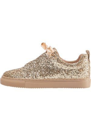 Lavtop sneaker dækket med guldglitter med beige gummisål og satin snørebånd på en hvid baggrund.