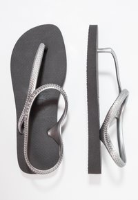 Hopeakuiset kumiset flip-flop-sandaalit, joissa on tekstuurilla varustetut hihnat, litteät mustat pohjat ja kuvioitu korostus hihnan reunoilla, nähtynä ylhäältä päin.