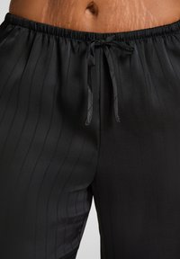 Zwarte satijnen broek met verticale ribbels, een elastische tailleband en een trekkoord. Zachte stof met een gladde afwerking.