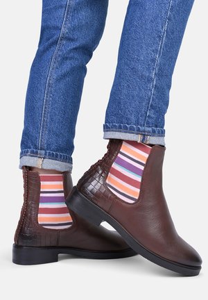 Brązowe skórzane botki za kostkę z błyszczącym wykończeniem, akcentami w fakturze krokodyla oraz elastycznymi bokami. Uzupełnione żywymi skarpetami w paski.