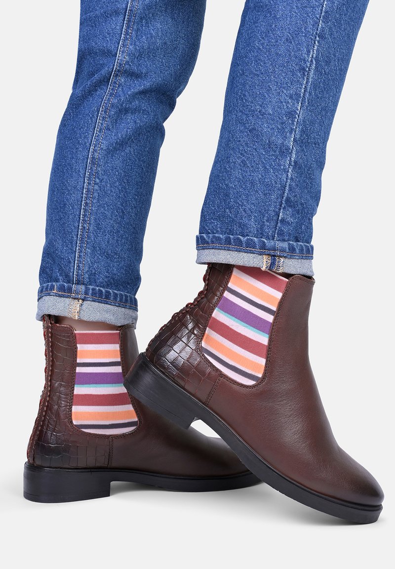 Brązowe skórzane botki za kostkę z błyszczącym wykończeniem, akcentami w fakturze krokodyla oraz elastycznymi bokami. Uzupełnione żywymi skarpetami w paski.