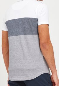 Polo tričko s krátkým rukávem v bílé, námořnické modři a světle šedé barvě. Má jednobarevný vršek, vodorovný pruhovaný vzor a hladkou texturu látky.