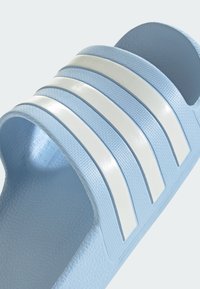 Light blue slide sandal made of textured rubber, featuring three white parallel stripes across the upper. Open-toe design with a contoured sole.