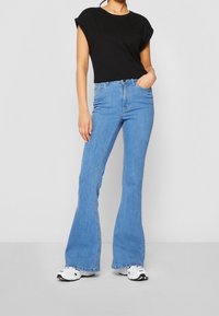 Černý, krátký rukáv, tričko s kulatým výstřihem, spárované s světle modrými, rozšířenými džínami s klasickým designem pěti kapes a zapínáním na knoflík.