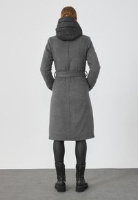 Palton lung din amestec de lână gri, cu o glugă căptușită neagră, talie cu curea și mâneci lungi. Are o croială dreaptă și o textură fină.