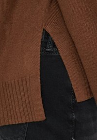 Brązowy dziergany sweter z prążkowanym dołem i bocznymi rozcięciami, zestawiony z czarnym denimem. Tekstura jest gładka z miękkim wykończeniem.