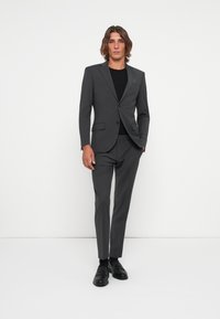 Grey suit with a fitted design, single-button blazer and matching trousers. Black undershirt and black shoes complete the look. Smooth texture.