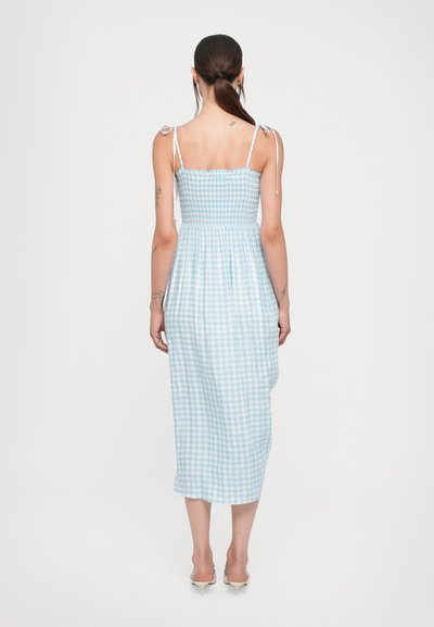 Sininen ja valkoinen ruudullinen midi-mekko, jossa on säädettävät solmimisolid, istuva vartalo ja virtaava hame. Sujuva puuvillakangas ruutukuviolla.