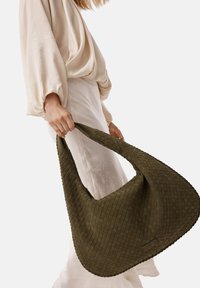 Sac fourre-tout tissé vert avec une forme douce et arrondie, ainsi qu'une surface texturée. La poignée est large et plate, offrant une prise en main confortable.