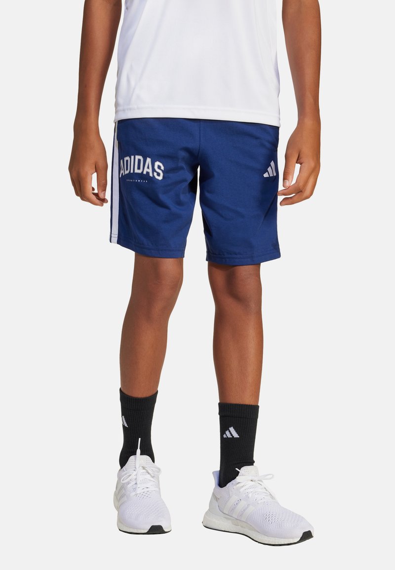 Pantalones cortos Adidas de color azul marino con logo blanco, fabricados con tejido ligero. Presentan rayas laterales y un ajuste cómodo. Se llevan con calcetines negros y zapatillas blancas.