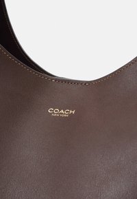 Sac à main Coach en cuir marron en gros plan montrant une texture lisse, des détails de couture et le logo doré Coach New York.