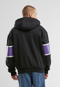 Black hooded sweatshirt with a purple and white stripe detail on the sleeves. Made from a soft fabric, featuring a relaxed fit and ribbed cuffs.