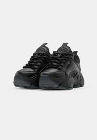 Scarpe sportive nere con tomaia in pelle testurizzata e rete, dotate di lacci prominenti, suole spesse e linguette sul tallone per una facile calzata.