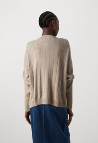 Beige Rippstrickpullover mit hohem Kragen, langen Ärmeln und lockerer Passform, kombiniert mit einem Jeansrock. Gestrickte Textur und Saumverarbeitung sichtbar.