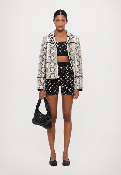 Snekkskinnmønstret jakke, svart crop top og shorts med måneprint. Svart håndveske og flate sko. Tekstilt stoff og tilpassede design.