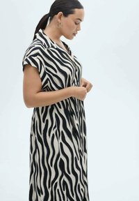 Rochie cu dungi zebra alb-negru, realizată dintr-un material moale, cu mâneci scurte, guler și o siluetă fluidă.
