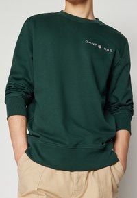 Grön sweatshirt i bomullsblandning med rundad halsringning, långa ärmar, ribbade ärmmuddar och broderad "GANT 1949" logotyp på bröstet.