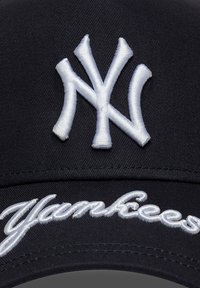 Black baseball cap with white embroidered "NY" logo and "Yankees" text on the front. Fabric is textured and smooth.