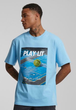 Himmelblå bomull T-skjorte med frontgrafikk av en tennisbane, en gul tennisball og teksten "PLAY LIT" i fete bokstaver.