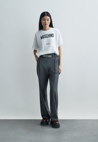 Valge t-särk musta "MOSCHINO Milano" kirjaga, kombineeritud hallide pükstega, millel on sobiv MOSCHINO vöö, ja massiivsete mustade platvormkingadega.