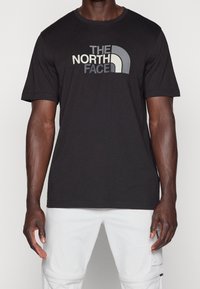 Czarna bawełniana koszulka z krótkim rękawem z logo "THE NORTH FACE" w białym i szarym kolorze. Klasyczny krój z okrągłym dekoltem. Gładka tekstura.