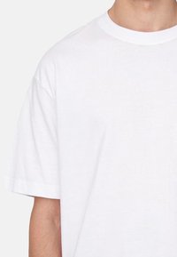 Weißes Baumwoll-T-Shirt mit kurzen Ärmeln und Rundhalsausschnitt, das eine glatte Textur und eine lockere Passform bietet. Keine Muster oder zusätzlichen Details sichtbar.