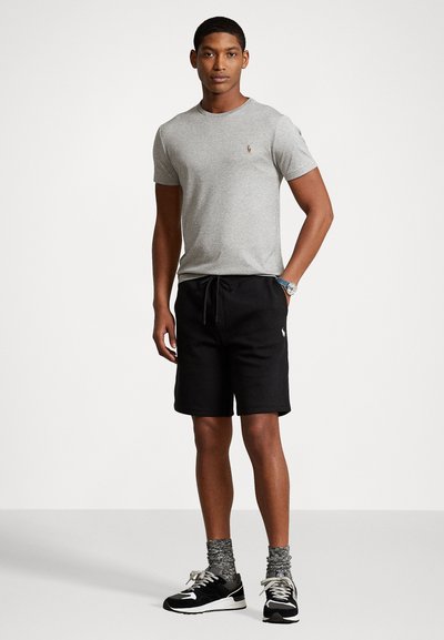 Tricou gri cu mânecă scurtă și un logo mic, asortat cu pantaloni scurți negri cu șnur. Accesoriile includ adidași gri și negri și sosete cu un imprimeu.