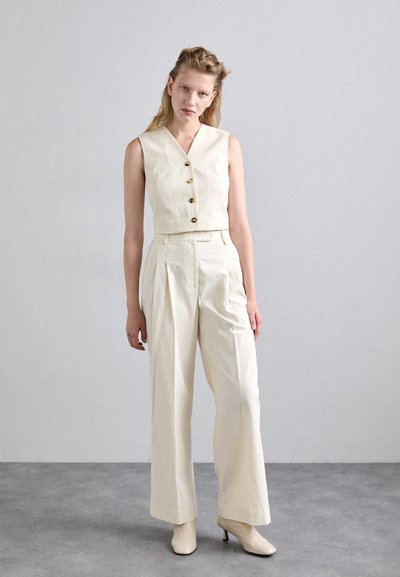 Ensemble coordonné en crème avec un haut cropped sans manches à boutons et un pantalon large taille haute. Assorti avec des talons neutres.