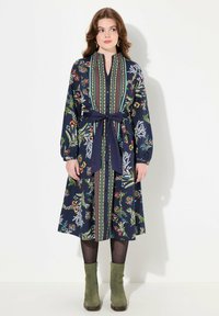 Robe florale marine à manches longues, devant boutonné et taille nouée. Caractéristiques de motifs colorés et de bordures contrastées. Longueur genou avec jupe évasée.