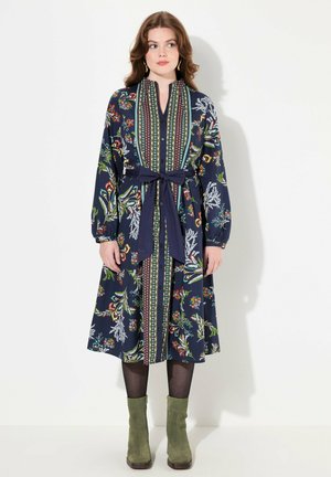 Vestido floral azul marino con mangas largas, botonera en el frente y cintura atada. Presenta patrones coloridos y un ribete en contraste. Largo hasta la rodilla con falda acampanada.