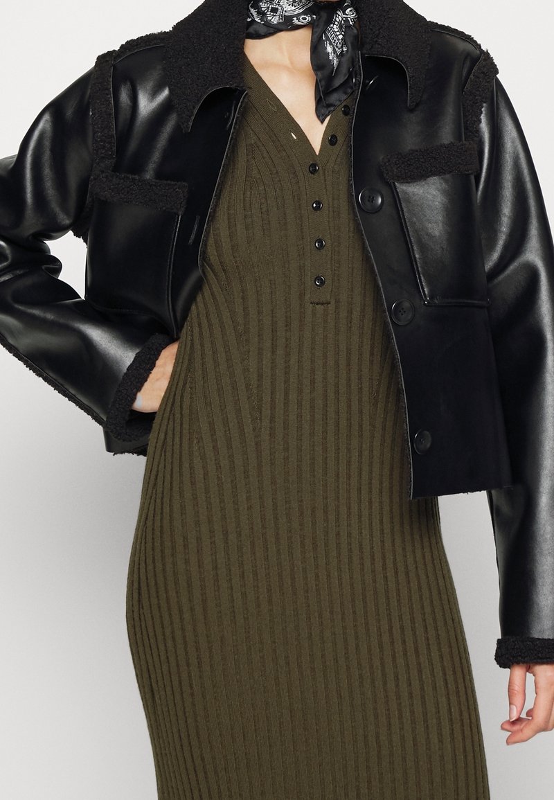 Svart läderjacka med shearling-accenter, med krage och framknappar. Bärs över en ribbad olivgrön klänning med henley-krage.