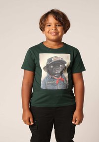 Groene katoenen t-shirt met een grafisch ontwerp van een hond in een spijkerjack en pet, met heldere ogen en een detail van een rode bandana.