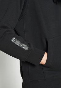 Svart sweatshirt med ribbad krage och muddar, med en reflekterande Nike-logotyp på ärmen och en stor känguruficka.