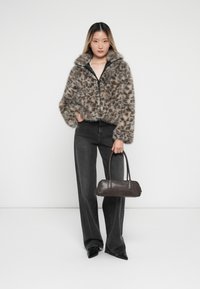 Faux fur jack met grijs en bruin luipaardpatroon, voorzien van een hoge kraag en ritssluiting, gecombineerd met high-waisted zwarte denim en een donkere handtas.