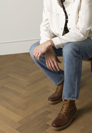 Bruine leren veterschoenen met een gestructureerde afwerking en robuuste zolen. Draagt het met lichtblauwe jeans en een crèmekleurige jas over een gestreept shirt.