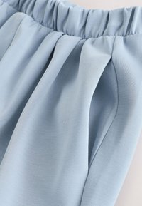Pantalon bleu clair avec ceinture élastique, poche latérale visible et texture de tissu douce.