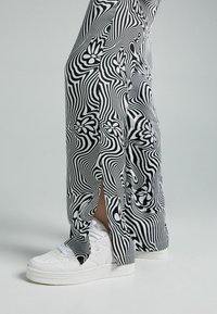 Svart och vit mönstrad byxa med en vågig design, med sidofickor, i kombination med vita sneakers med perforerade detaljer.