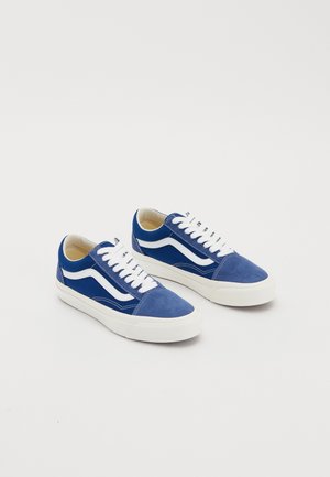 Paire de baskets basses bleues et blanches avec des lacets blancs et des semelles en caoutchouc sur un fond blanc uni.