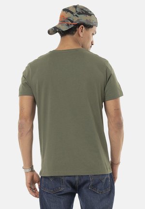 T-shirt en coton vert olive avec un col rond, des manches courtes et un ourlet droit, associé à un jean en denim bleu foncé et une casquette camouflage.