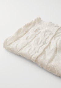 Πλεκτό cardigan από μαλακό λευκό μαλλί, με ριγωτό γιακά και τρία κουμπιά μπροστά. Η υφή προσφέρει βάθος στο ύφασμα.