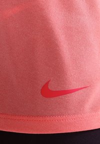 Korale t-shirt Nike z gładką fakturą, krótkimi rękawami i wyraźnym czerwonym logo blisko dolnej krawędzi. Casualowy design z okrągłym dekoltem.