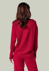 Roter Strickpullover mit lockerer Passform, gerippten Bündchen und Saum, von hinten gezeigt. Die Textur wirkt weich und angenehm.