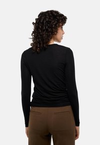 Haut noir à manches longues affichant un design ajusté et une texture lisse, associé à un pantalon ajusté marron avec poches arrière.