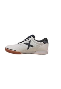 Zapatilla blanca con acentos negros, que presenta un diseño acolchado, lengüeta de malla y suela de goma. Incluye un prominente logotipo negro en forma de X.